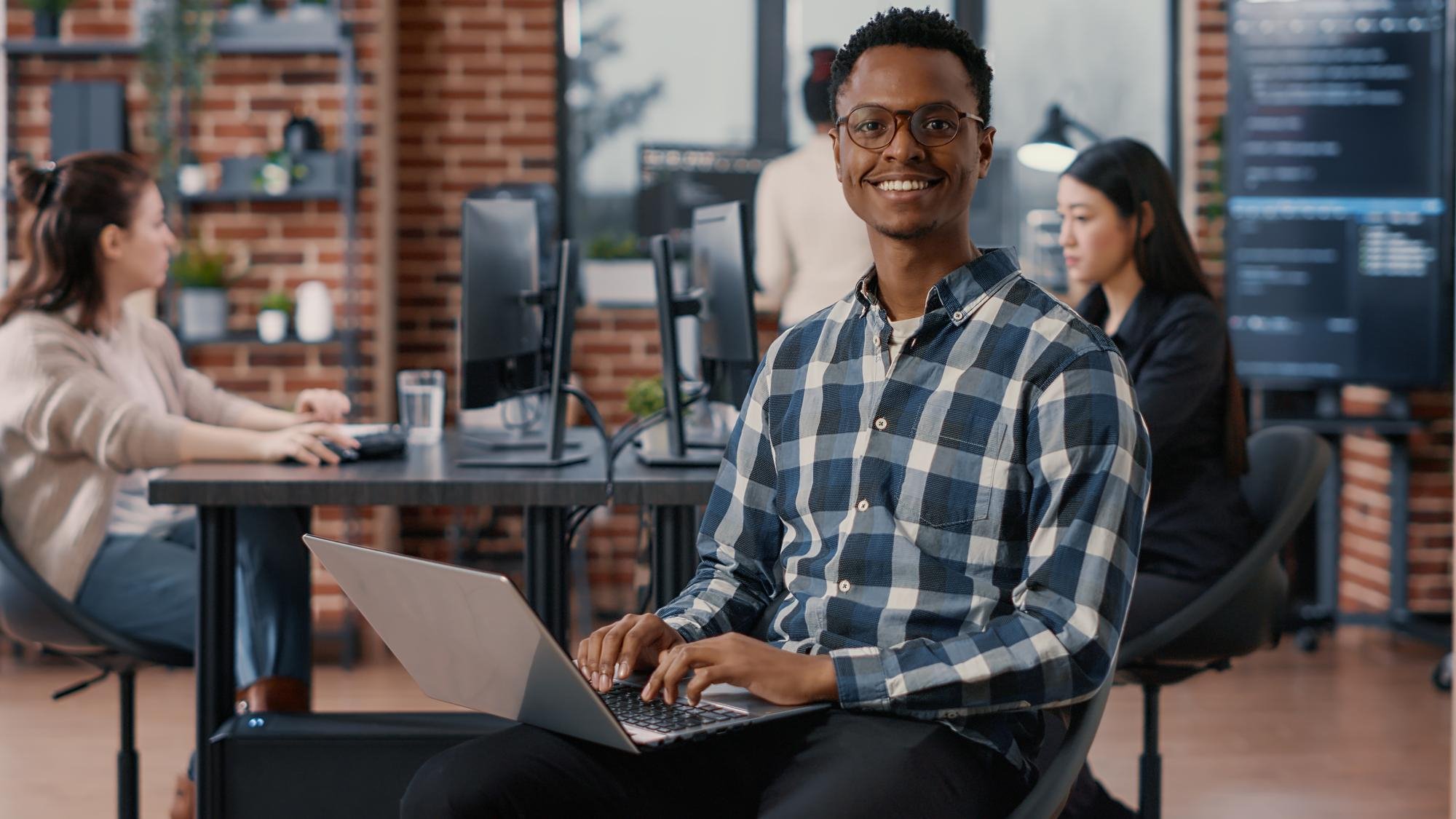 portrait-artificial-intelligence-app-developer-sitting-down-typing-laptop-fixing-glasses-looking-up-smiling-camera-programer-using-portable-computer-innovating-cloud-computing