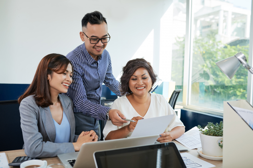 two-asian-female-one-male-colleagues-discussing-document-together-office